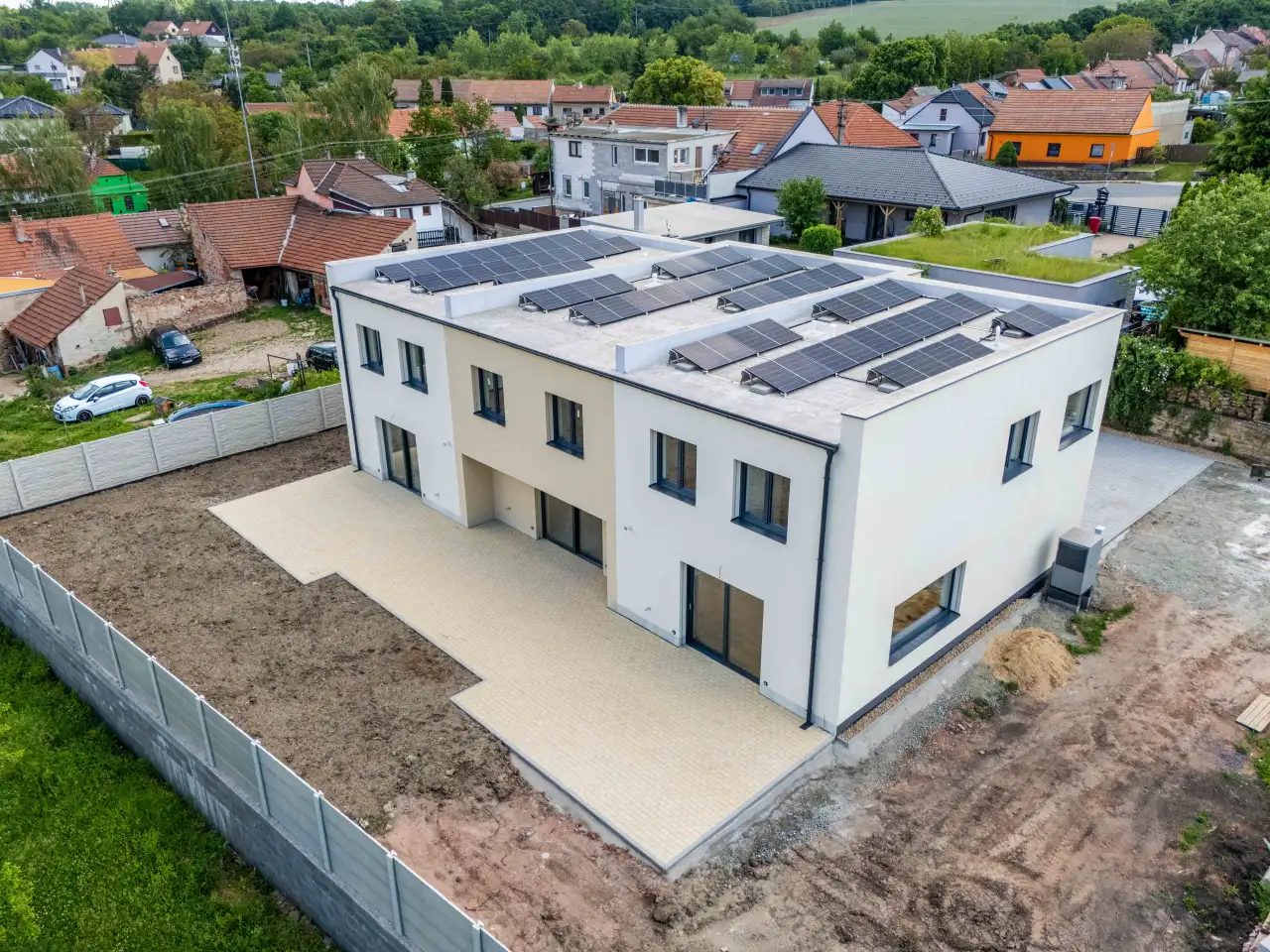 Letecký pohled na trojdům s fotovoltaikou a krajinou v pozadí